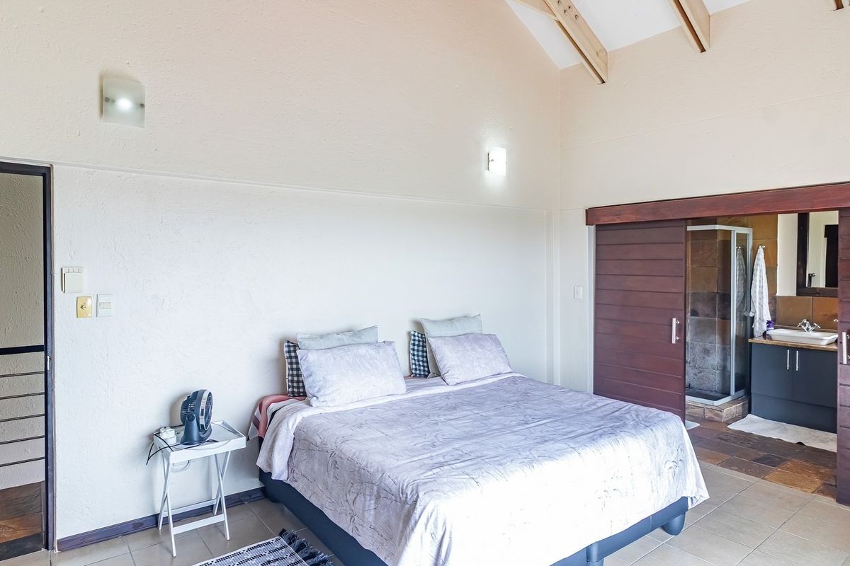 Spacious bedroom featuring a vaulted ceiling with exposed timber rafters, tiled flooring, and a sliding timber door leading to an en-suite bathroom.