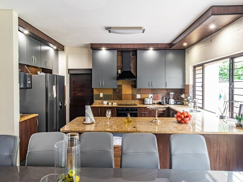 A well-appointed kitchen featuring granite countertops, modern grey cabinetry, built-in appliances, and a functional breakfast bar layout.