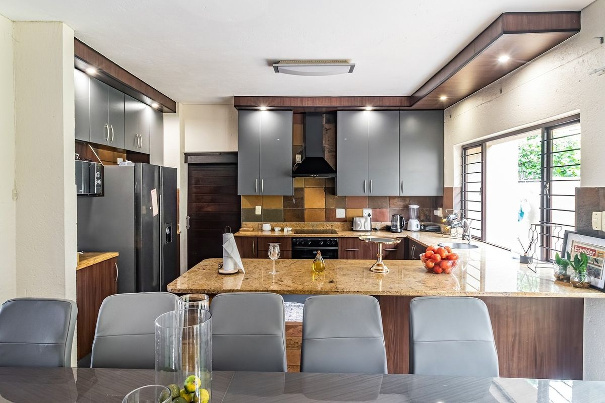 A well-appointed kitchen featuring granite countertops, modern grey cabinetry, built-in appliances, and a functional breakfast bar layout.