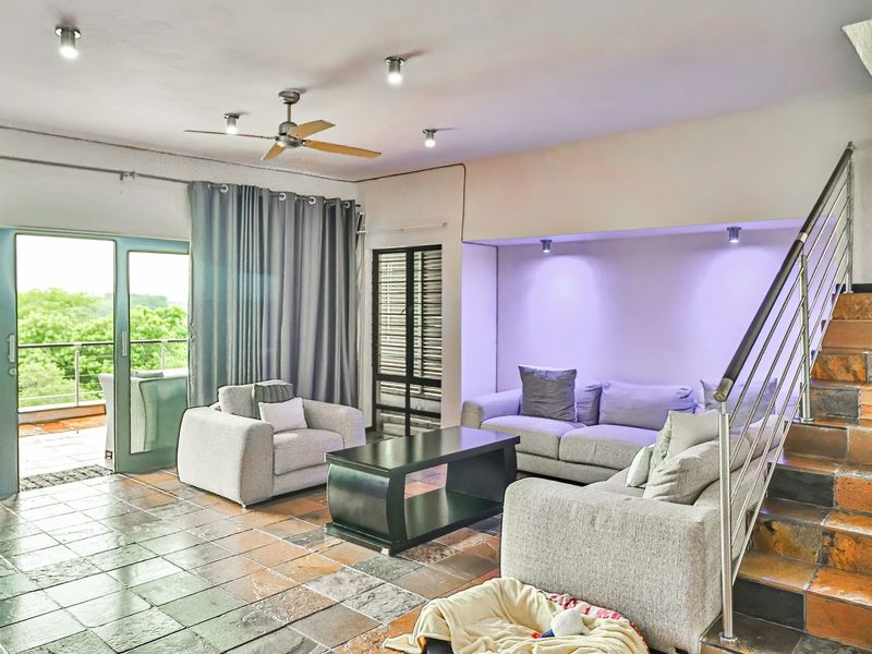 Spacious living room featuring tiled flooring, a staircase with metal railing, recessed lighting, and direct access to an outdoor balcony through sliding glass doors.