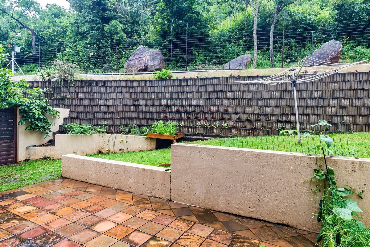 A terraced rear garden featuring a paved patio area, concrete retaining walls, and an electric fence perimeter.