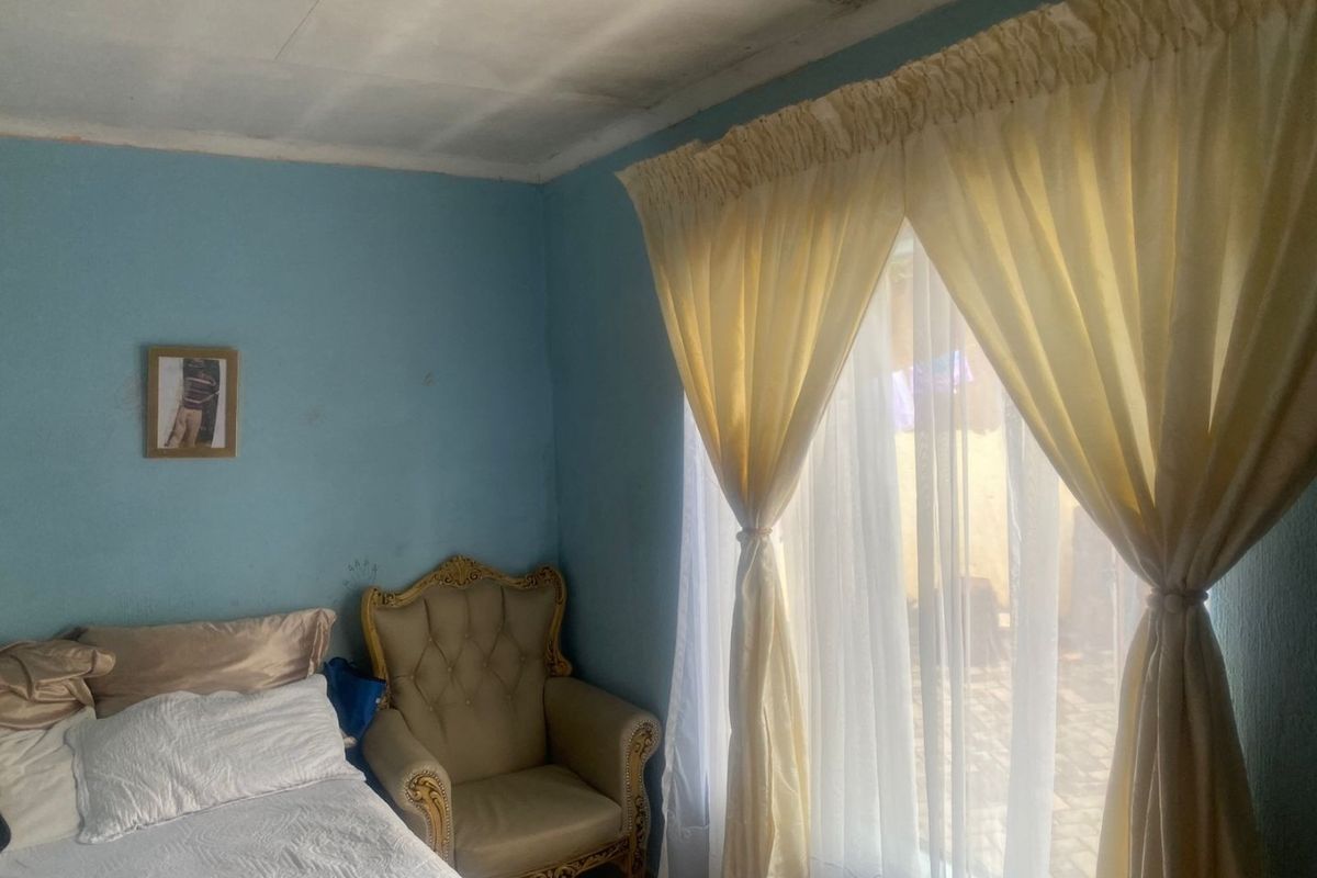 A bedroom featuring a large window with natural light, tiled flooring, and visible ceiling water damage requiring maintenance.