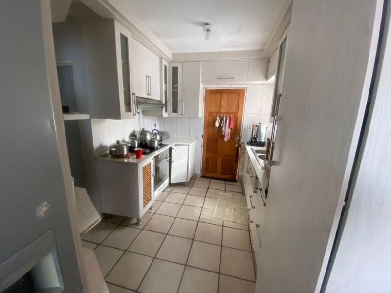 A functional galley-style kitchen featuring tiled flooring, built-in cabinetry, and integrated cooking appliances, offering potential for modernization and cosmetic updates.