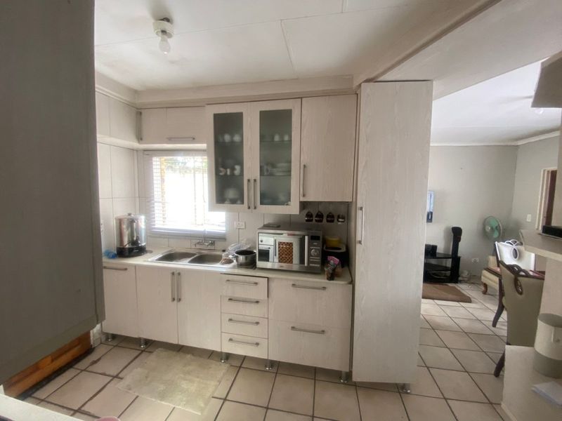 A functional kitchen featuring light-toned built-in cabinetry, a double bowl sink, and tiled flooring, offering a practical layout with adjacent living space.