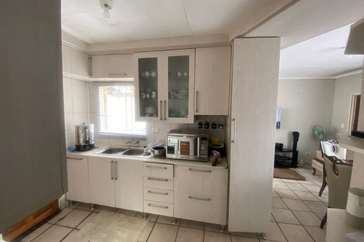 A functional kitchen featuring light-toned built-in cabinetry, a double bowl sink, and tiled flooring, offering a practical layout with adjacent living space.