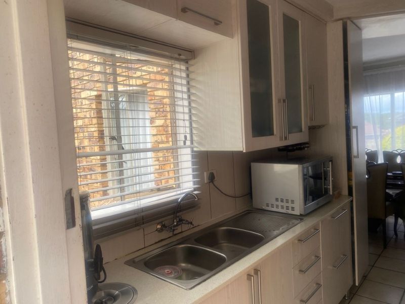 A functional kitchen area featuring light-toned cabinetry, a double bowl stainless steel sink, and ample storage space with glass-fronted wall units.