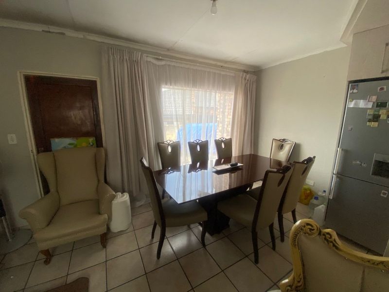 A dining room area featuring tiled flooring and large windows with curtain rails, providing a functional space for family meals.