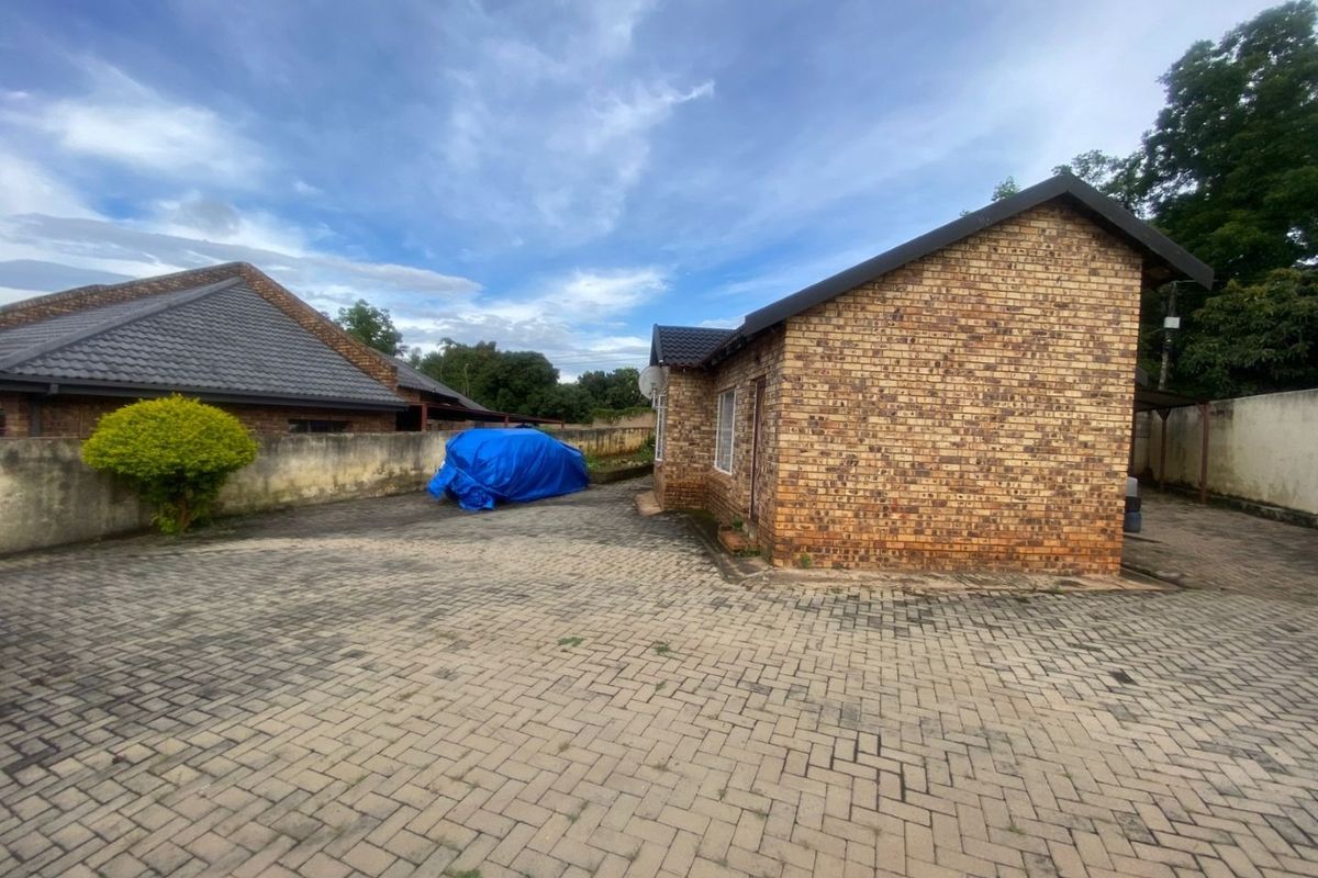 Rear exterior view of a face brick house featuring a large paved driveway and surrounding boundary walls.