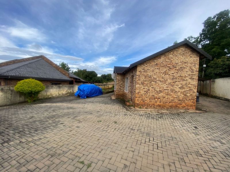 Rear exterior view of a face brick house featuring a large paved driveway and surrounding boundary walls.