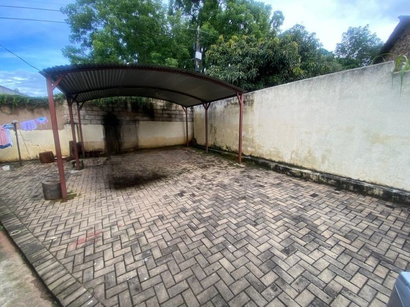 An outdoor paved area featuring a covered carport structure with metal roofing and perimeter boundary walls, suitable for parking or outdoor utility use.