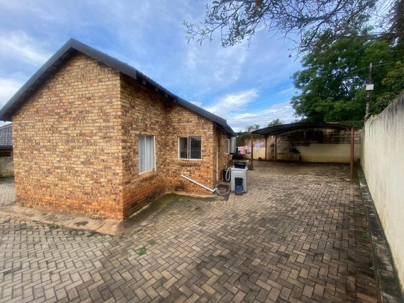 Rear exterior view of a face brick house featuring a paved driveway, carport, and boundary wall.