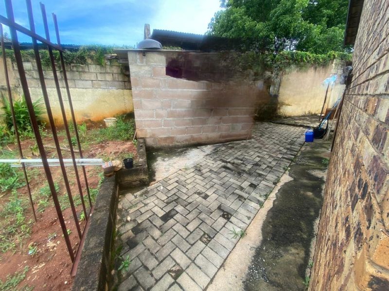 A rear exterior area featuring paved walkways, brick boundary walls, and a small concrete block structure requiring maintenance and landscaping improvements.