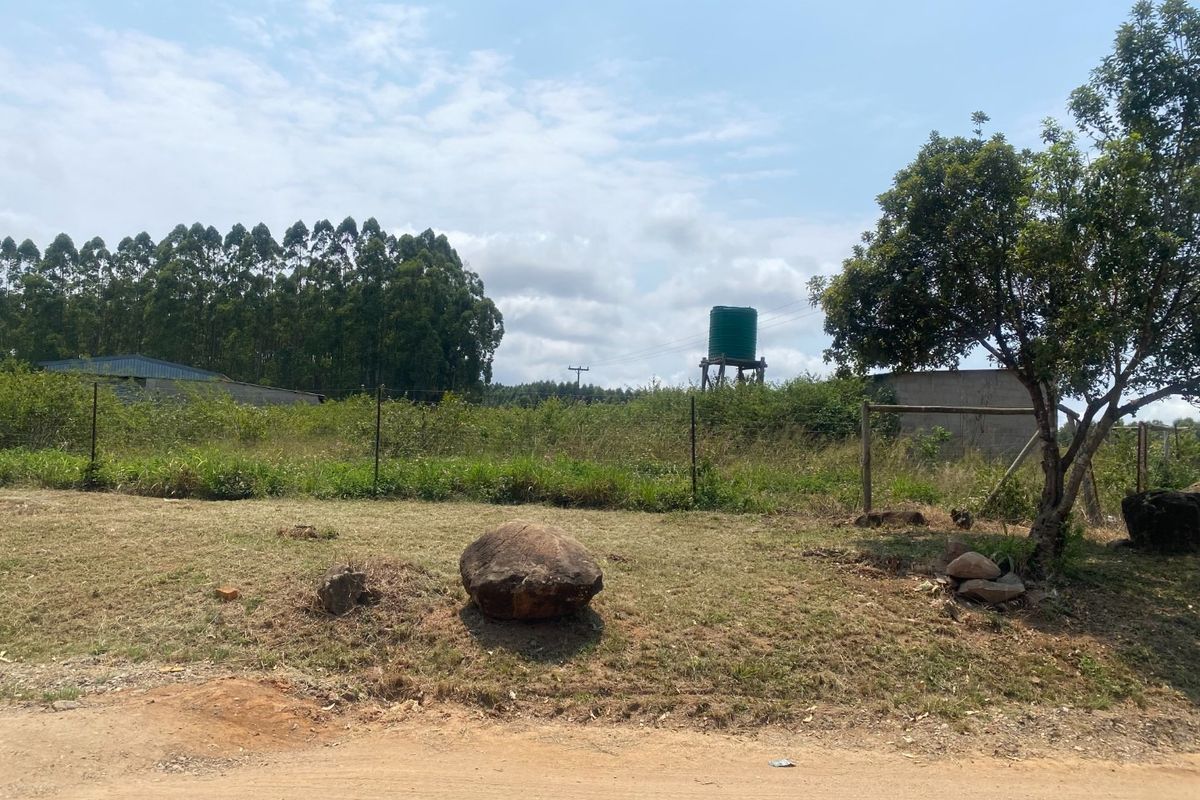A view of the small holding grounds featuring a water tank, wire fencing, and natural vegetation with an outbuilding in the background.