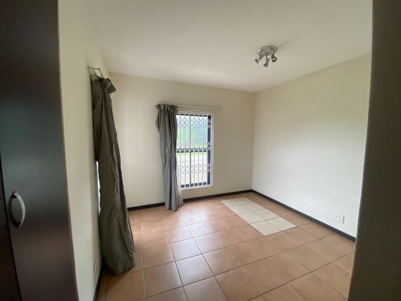A vacant bedroom featuring tiled flooring, a security gate on the window, and a built-in cupboard.