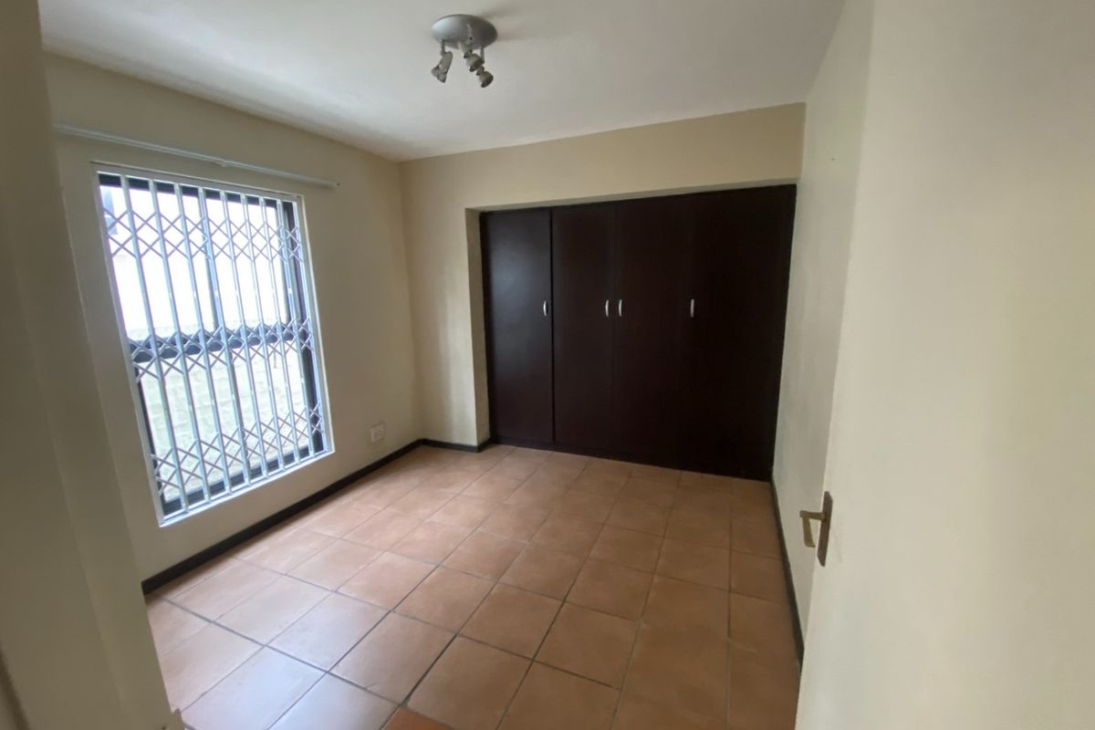 An empty bedroom featuring tiled flooring, built-in dark wood cupboards, and a window fitted with a security gate.