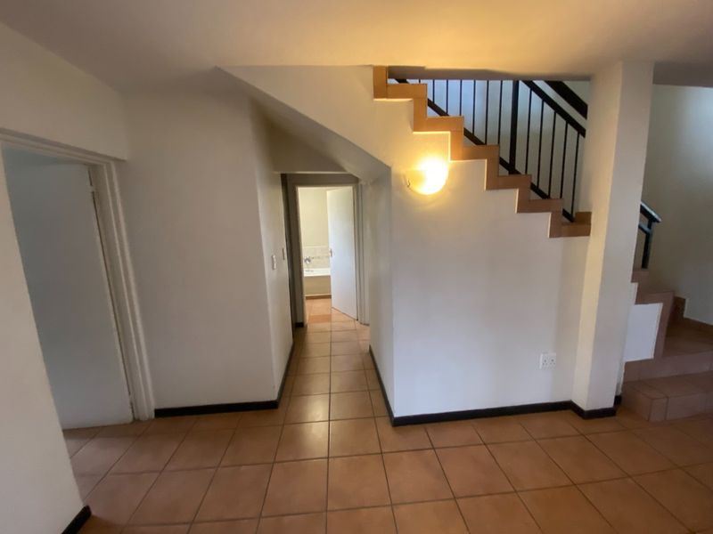 A tiled hallway featuring a staircase with a metal balustrade, leading towards an adjacent room with visible bathroom fixtures.