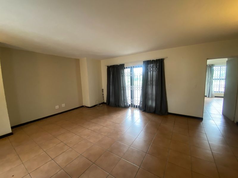 A spacious, empty living room featuring neutral tiled flooring and a sliding glass door with security gate, providing access to the exterior.