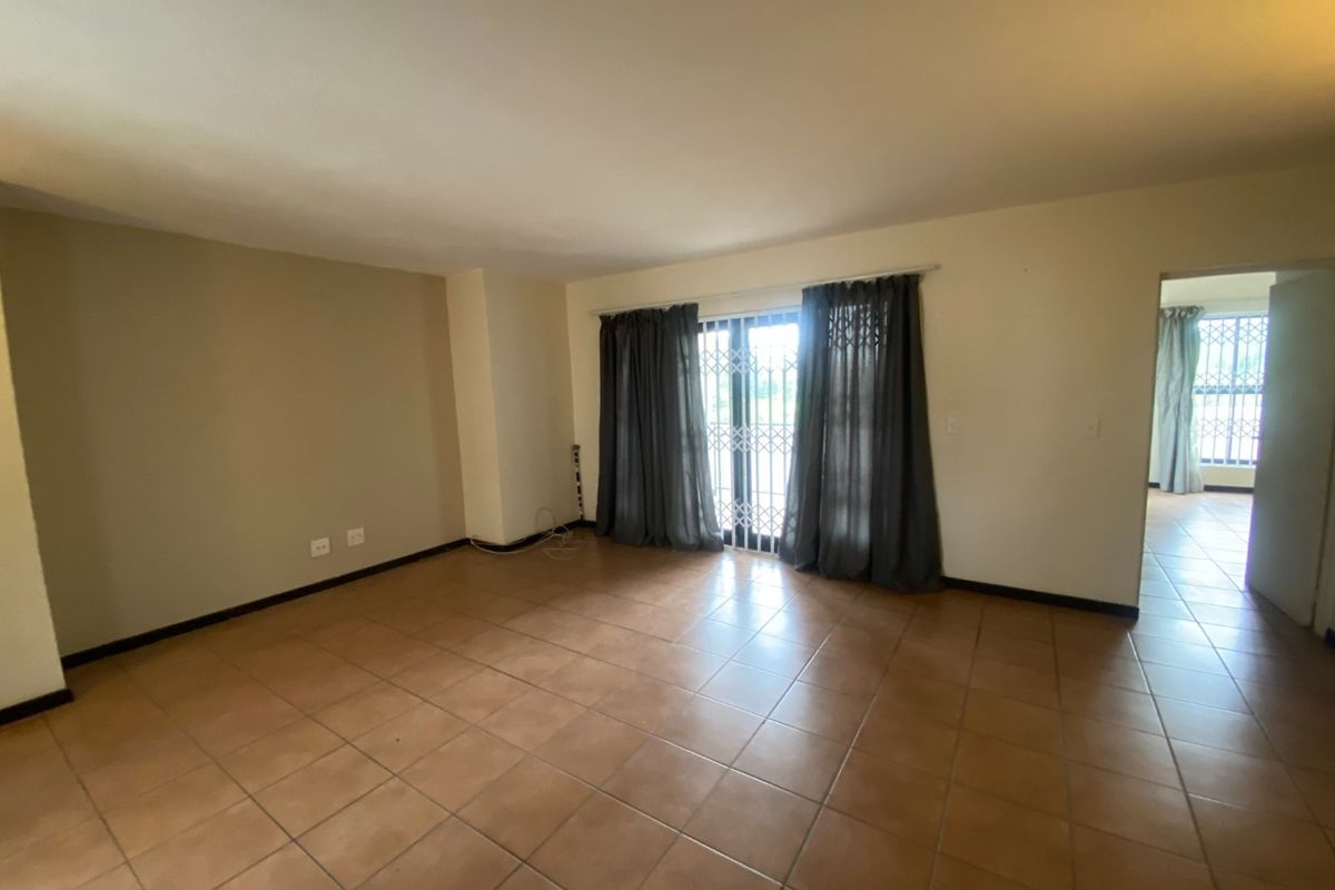 A spacious, empty living room featuring neutral tiled flooring and a sliding glass door with security gate, providing access to the exterior.