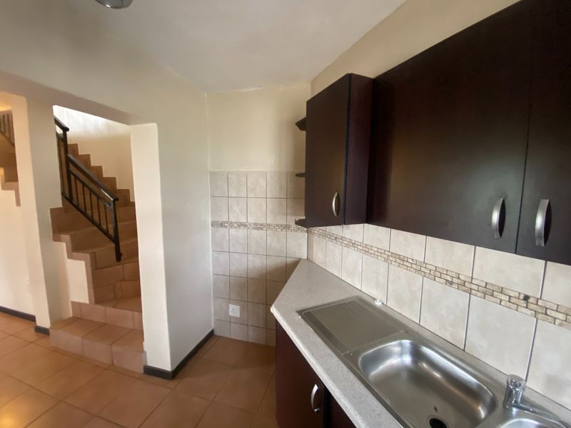A functional kitchen area featuring dark built-in cabinetry, a stainless steel sink, and tiled backsplash, adjacent to an internal staircase.