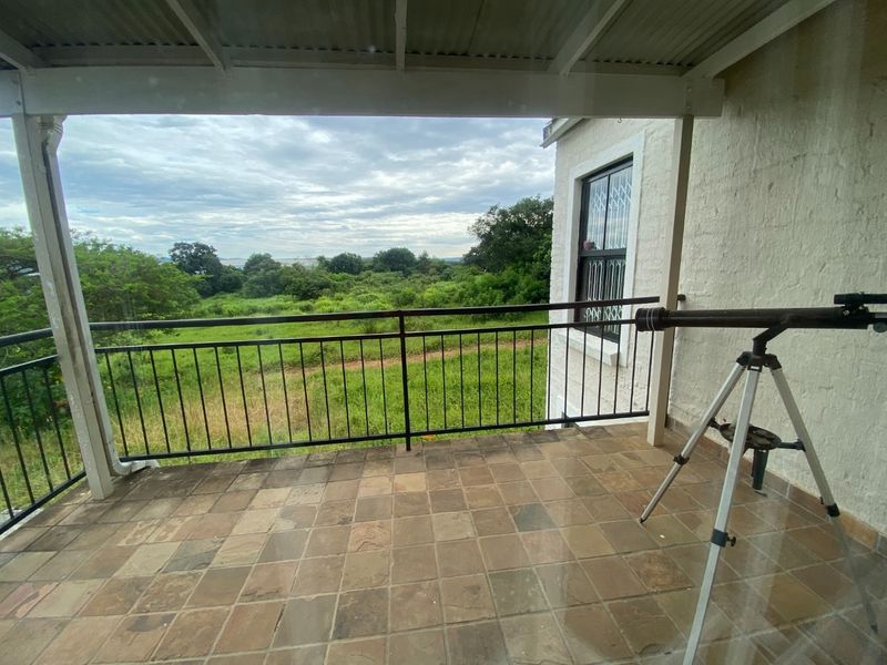 A covered balcony featuring tiled flooring and a metal balustrade, offering an open view of the surrounding natural landscape.