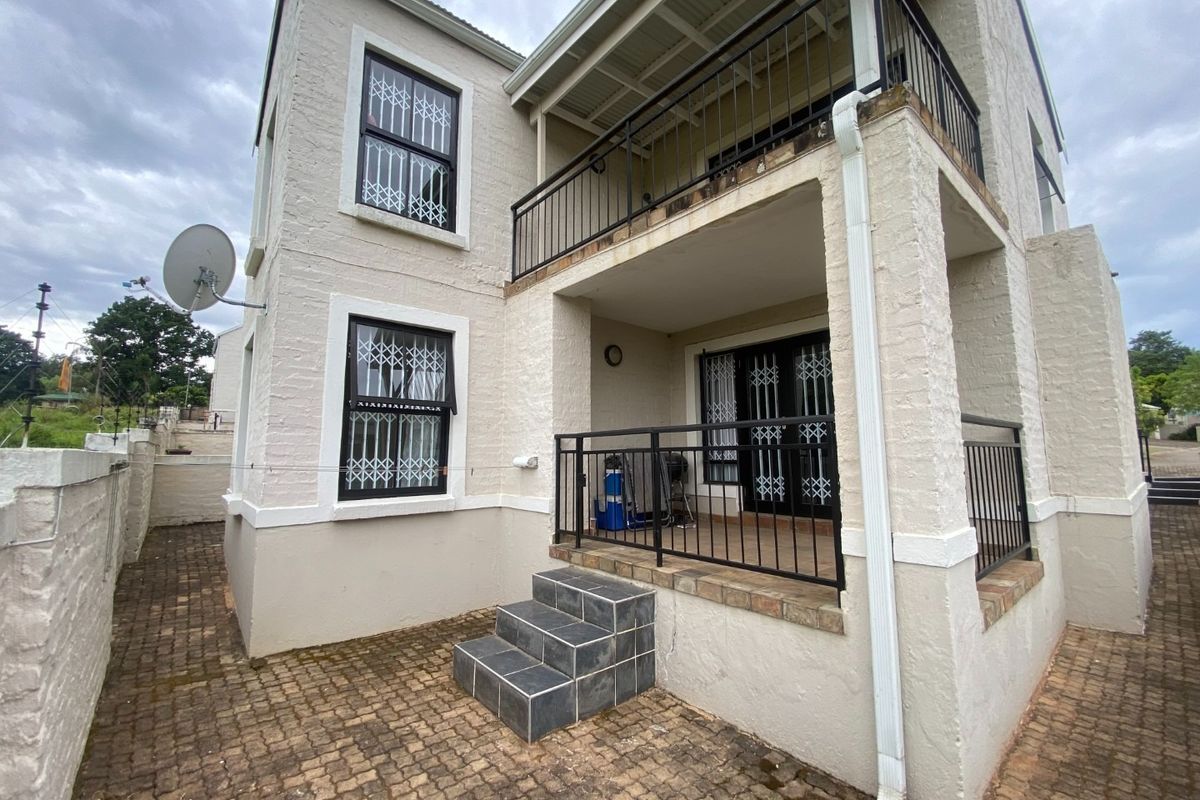 Rear view of the property featuring a paved patio area, a covered balcony with metal railings, and security gates on windows and doors.