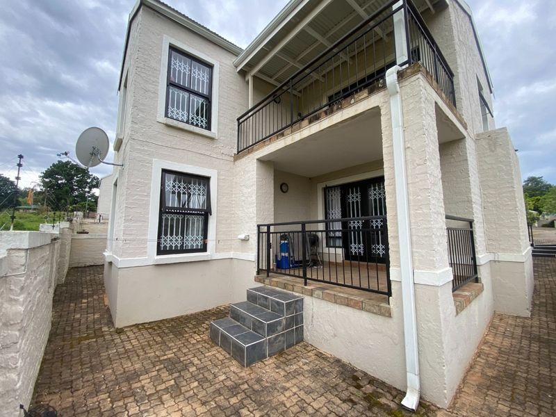 Rear view of the property featuring a paved patio area, a covered balcony with metal railings, and security gates on windows and doors.