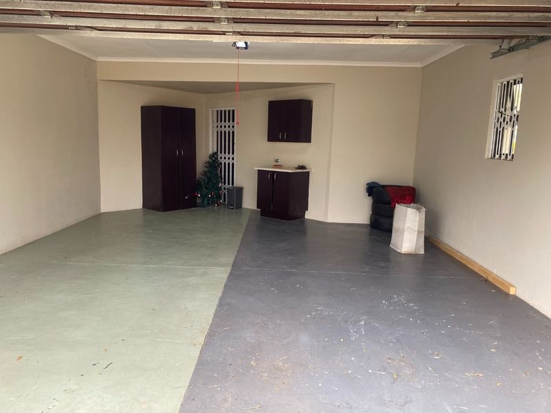 Spacious double garage featuring painted concrete flooring, built-in storage cabinetry, and secure access points with security gates and window bars.