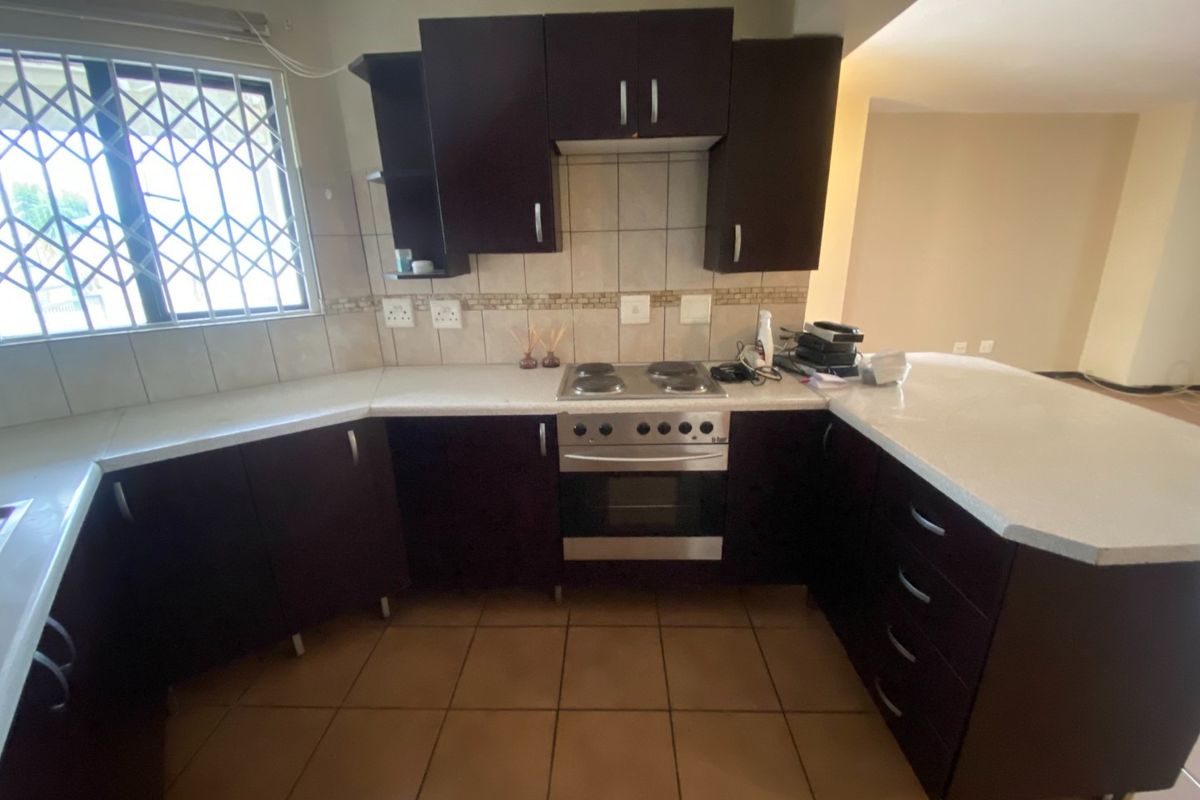 A functional kitchen featuring dark cabinetry, a built-in electric stove and oven, tiled backsplash, and a breakfast counter, with tiled flooring throughout.