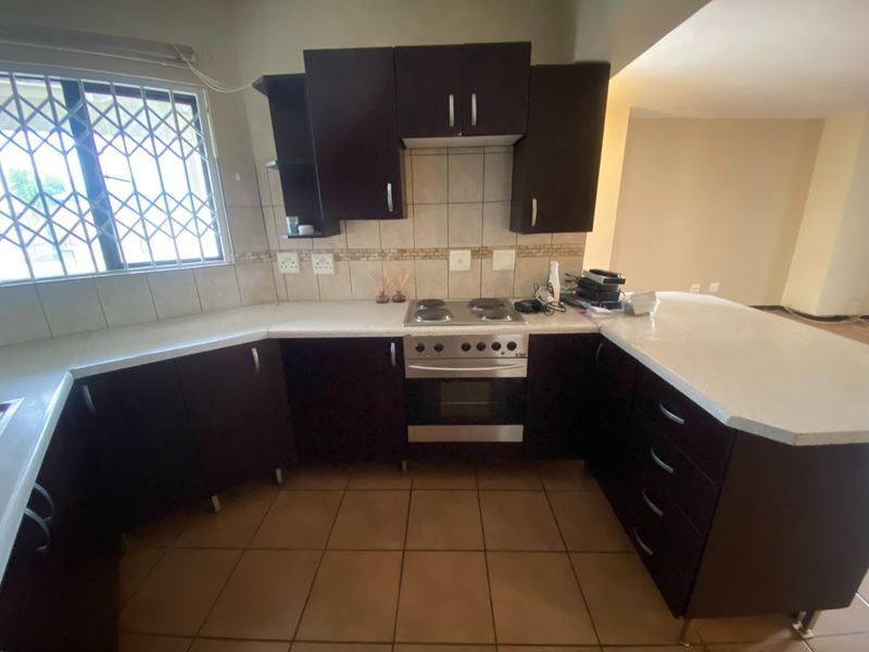 A functional kitchen featuring dark cabinetry, a built-in electric stove and oven, tiled backsplash, and a breakfast counter, with tiled flooring throughout.