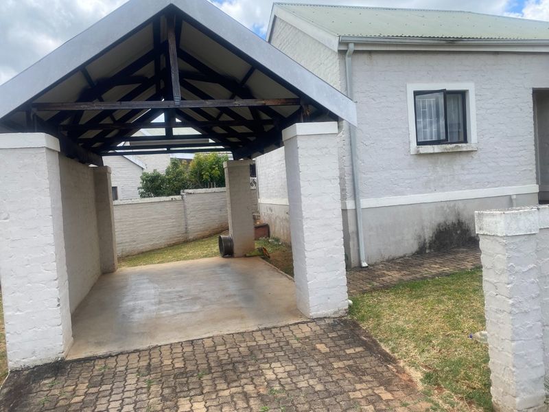 A covered carport structure with brick pillars and a paved driveway, situated alongside the main house exterior.