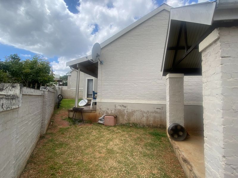 Rear exterior view of the property featuring a covered patio, brick boundary wall, and visible signs of exterior wall maintenance required.