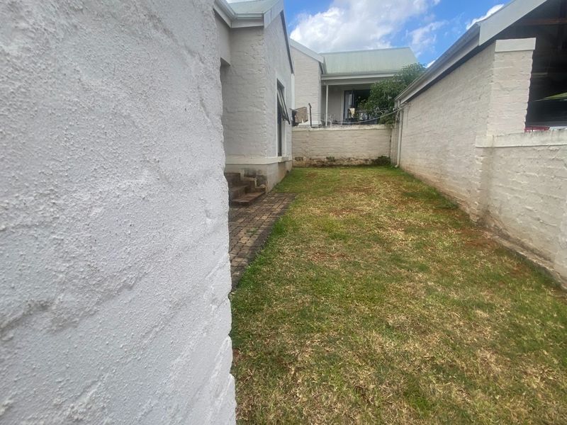 A rear garden area featuring a lawn, paved walkway, and painted brick boundary walls.