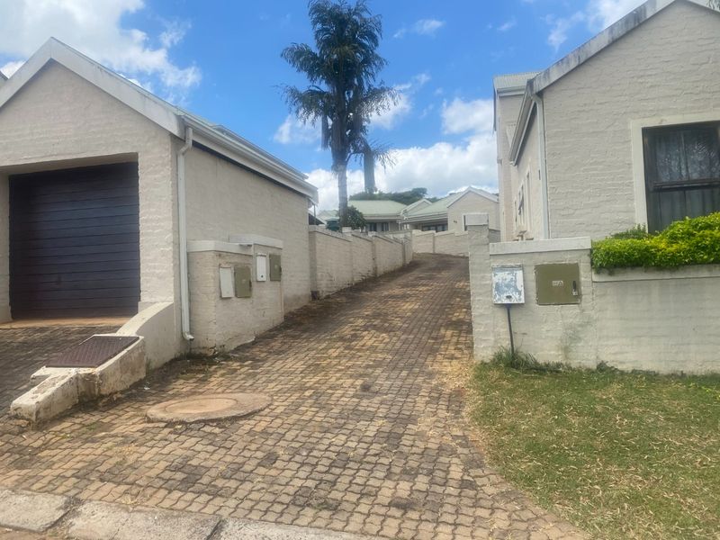 Front view of the property featuring a paved driveway leading to a garage, enclosed by boundary walls with utility access points.