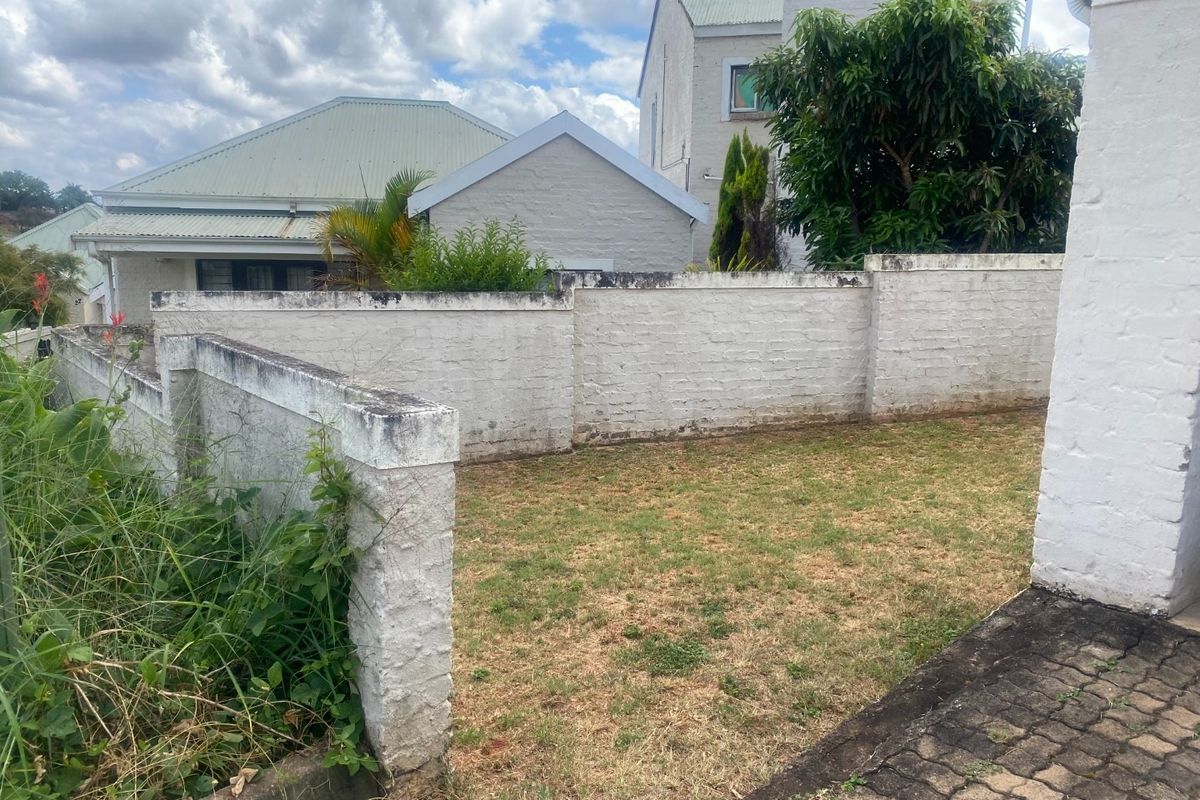 A rear garden area featuring a brick boundary wall, a small lawn, and a paved walkway, showing signs of weathering and maintenance needs.