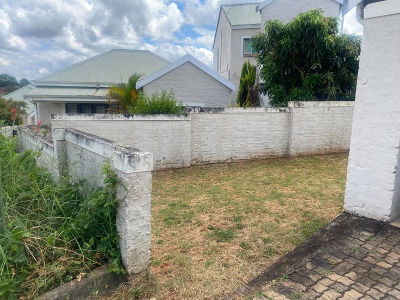 A rear garden area featuring a brick boundary wall, a small lawn, and a paved walkway, showing signs of weathering and maintenance needs.