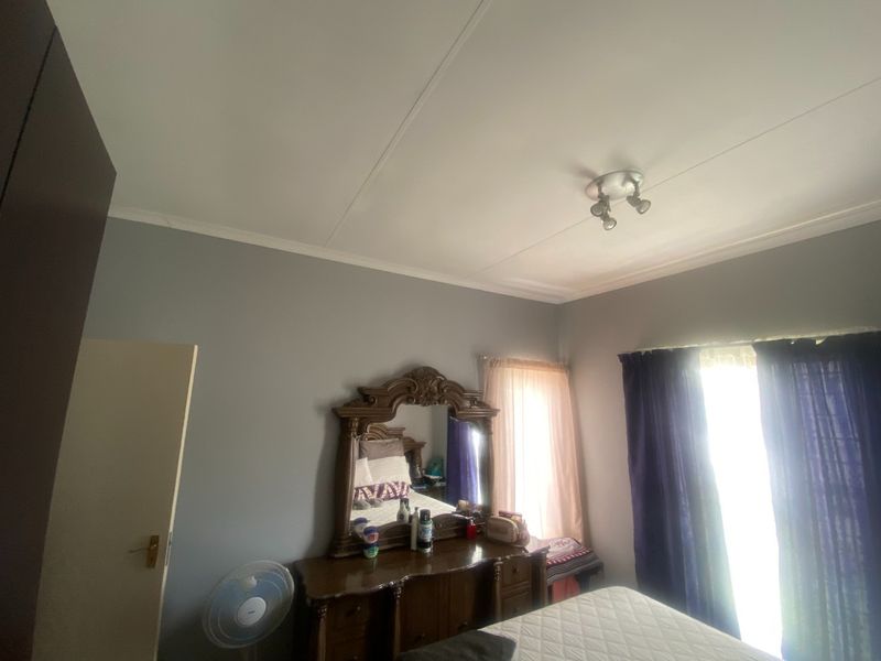 A bedroom featuring grey walls, coving, and a ceiling-mounted spotlight fixture, providing a neutral base for interior design.