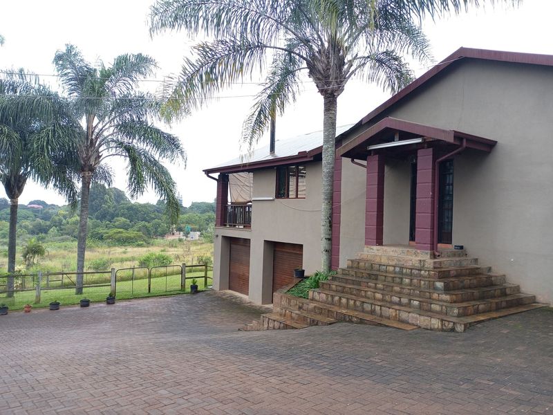 Front elevation of a small holding property featuring a paved driveway, stone entrance staircase, double garage, and an upper-level balcony overlooking the landscape.