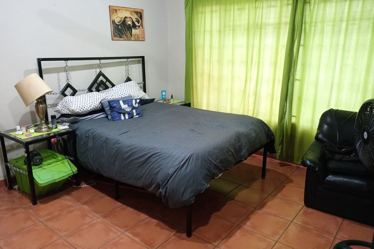 A functional bedroom featuring tiled flooring and large windows with curtain rails, providing a neutral base for potential interior updates.