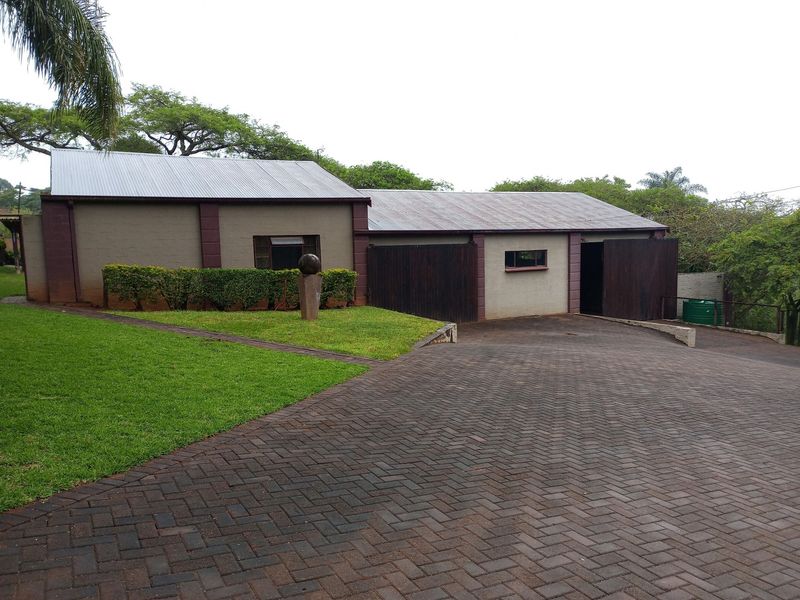 Front view of the property featuring a large paved driveway, established lawn, and a structure with a corrugated metal roof and timber garage doors.