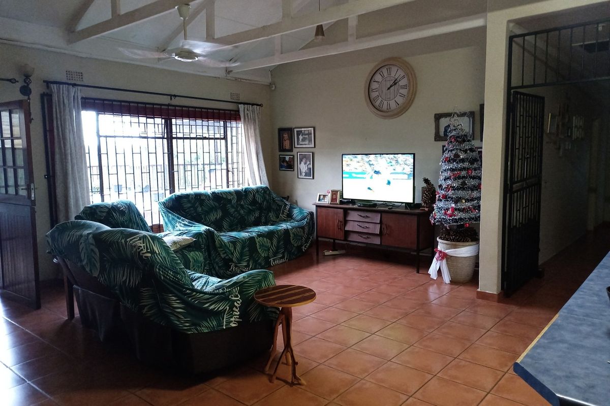 Spacious living room featuring exposed rafters, ceiling fan, and tiled flooring, with security bars on windows and a security gate at the entrance.