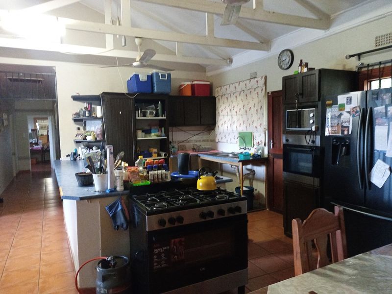 Open-plan kitchen area featuring exposed roof trusses, tiled flooring, gas stove, and built-in oven, offering a functional layout with potential for modern updates.