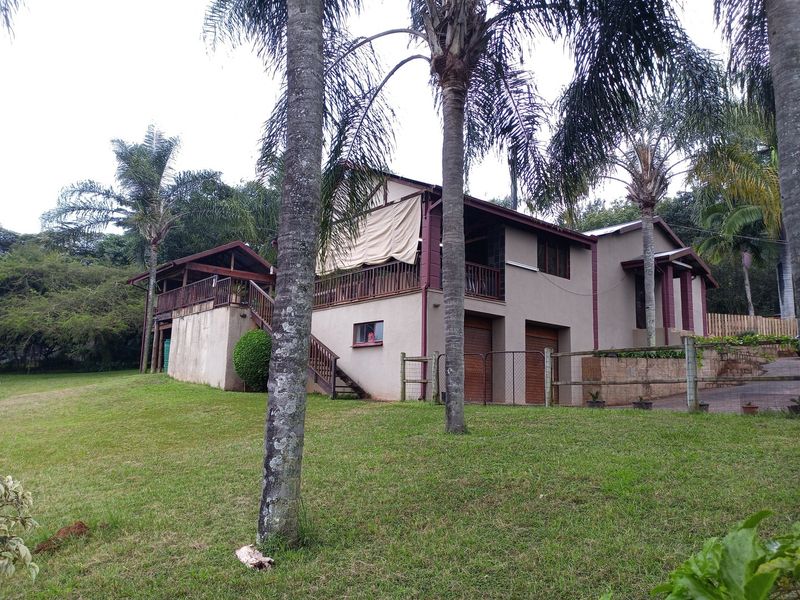 Rear view of the property featuring a raised wooden deck with balustrades, external staircase, and lower-level garage access set within a spacious garden.