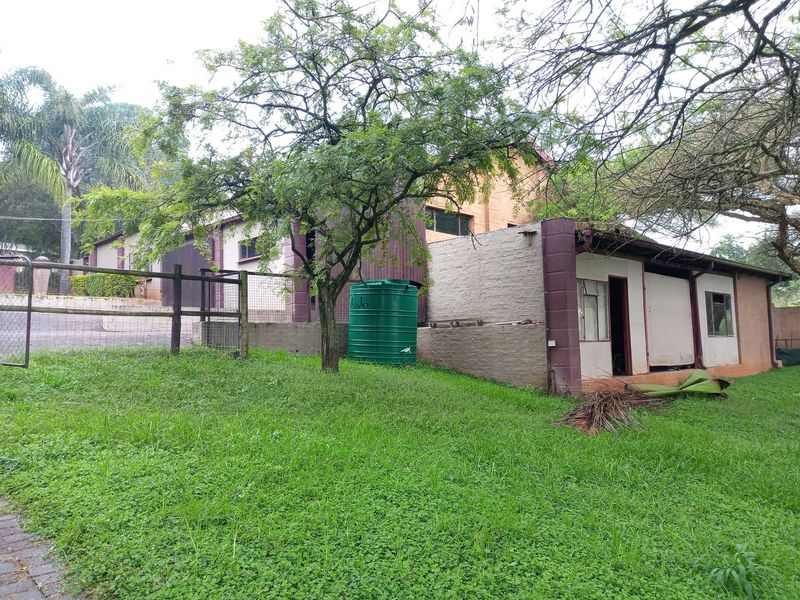 Rear view of the property showing a brick structure, water storage tank, and surrounding garden area with wire fencing.