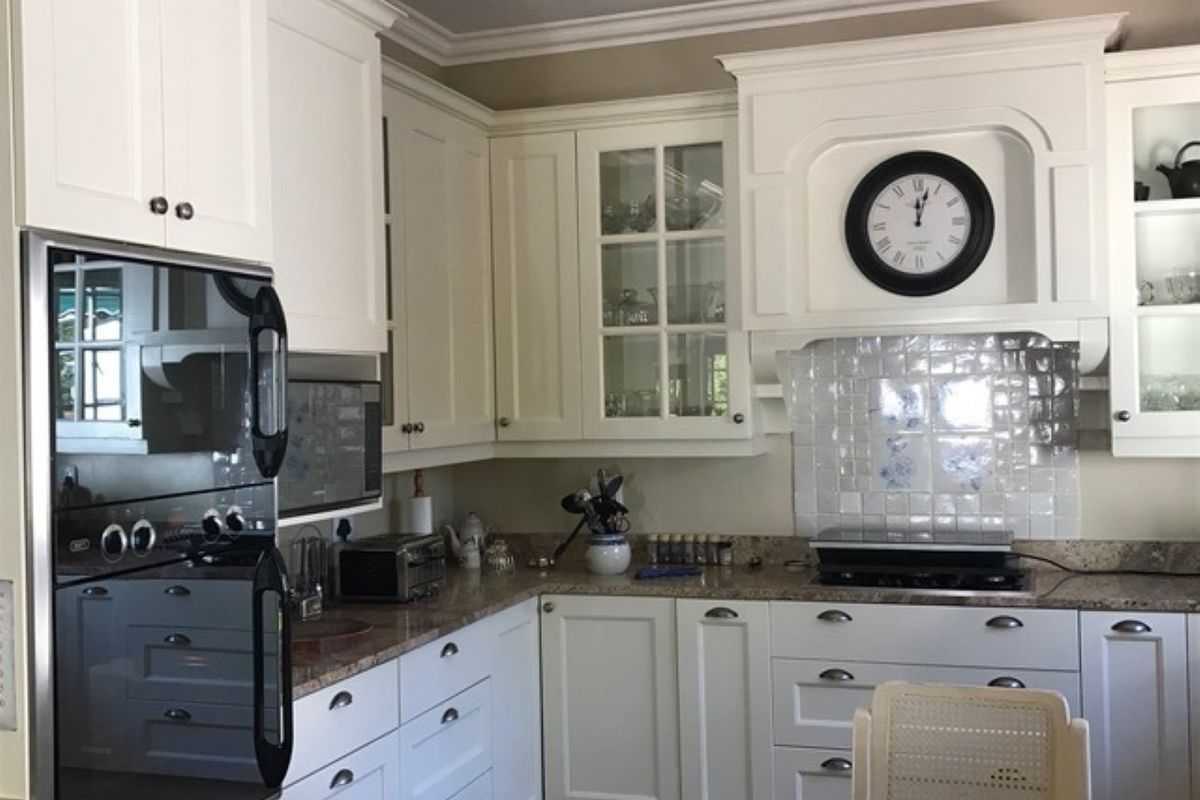 A well-maintained kitchen featuring white cabinetry, granite countertops, a tiled backsplash, and integrated appliances including a built-in oven and hob.