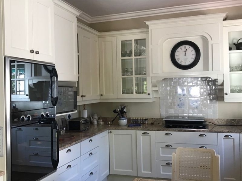 A well-maintained kitchen featuring white cabinetry, granite countertops, a tiled backsplash, and integrated appliances including a built-in oven and hob.