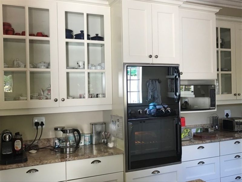 A well-maintained kitchen featuring white shaker-style cabinetry, glass-front display cupboards, granite countertops, and integrated stainless steel oven and microwave appliances.
