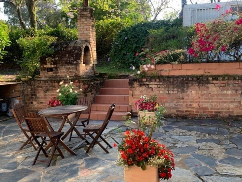 Outdoor patio area featuring a rustic brick pizza oven, stone paving, and tiered brick retaining walls with integrated stairs leading to the garden.