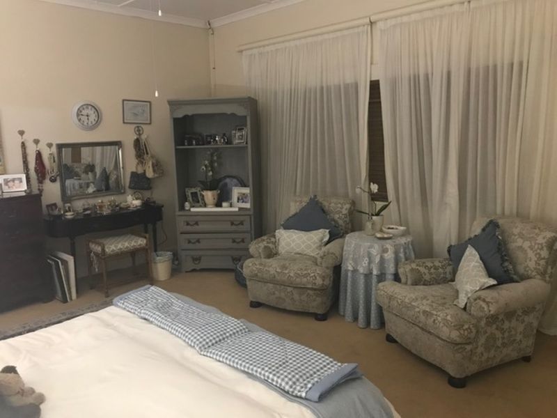 A carpeted bedroom featuring a ceiling fan and large window with sheer curtains, offering a comfortable and functional living space.