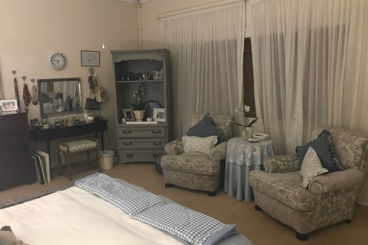 A carpeted bedroom featuring a ceiling fan and large window with sheer curtains, offering a comfortable and functional living space.
