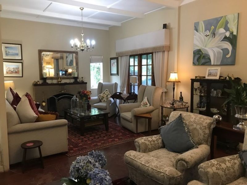A cozy living room featuring a traditional fireplace, exposed beam ceiling, and timber flooring, with direct access to the garden through french doors.